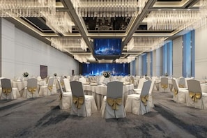 Une salle de banquet avec des tables rondes, des chaises et une scène dotée d’un décor de fond bleu.