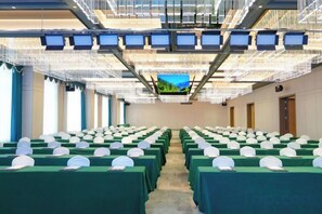 Un salón de conferencias con filas de mesas, cada una con una cubierta blanca sobre el mantel, y una pantalla grande al frente.