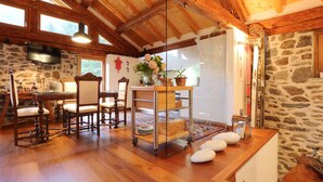 Un intérieur rustique en bois, avec un mur en pierre, un coin repas doté de chaises anciennes et une table en verre agrémentée de plantes en pot.