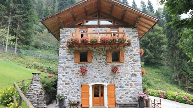 Un bâtiment en pierre avec des volets en bois, un balcon orné de jardinières et un toit en bois.