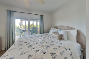 A bedroom with a large bed, a view of the outdoors, and a ceiling fan. - Sunshiny Daze by Topsail Realty (Holly Ridge)