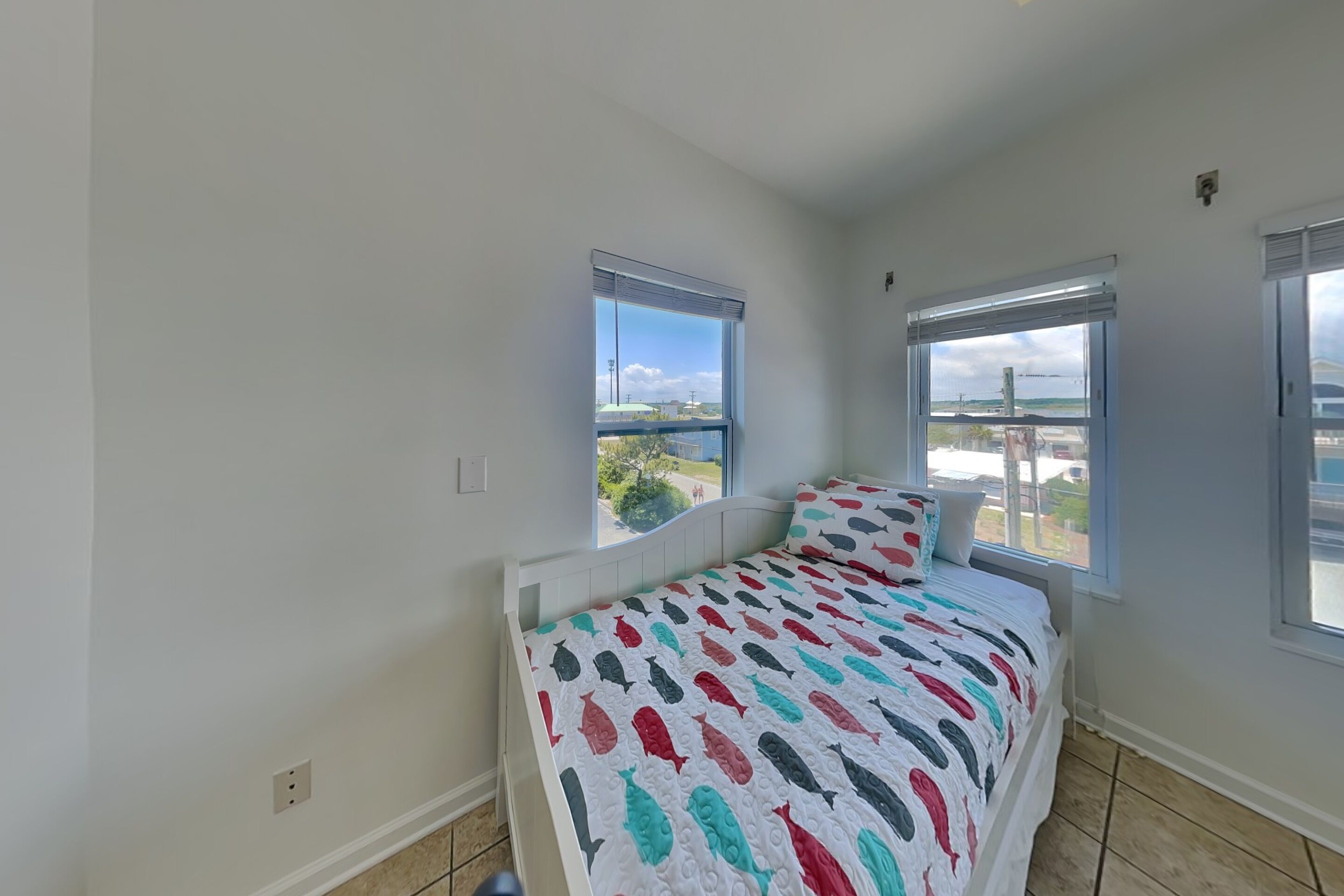A bedroom with a bed, two windows, and a view of the outdoors.