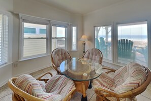 A dining area with wicker chairs, a glass table, and large windows with a view of the ocean. - Sunshiny Daze by Topsail Realty (Holly Ridge)