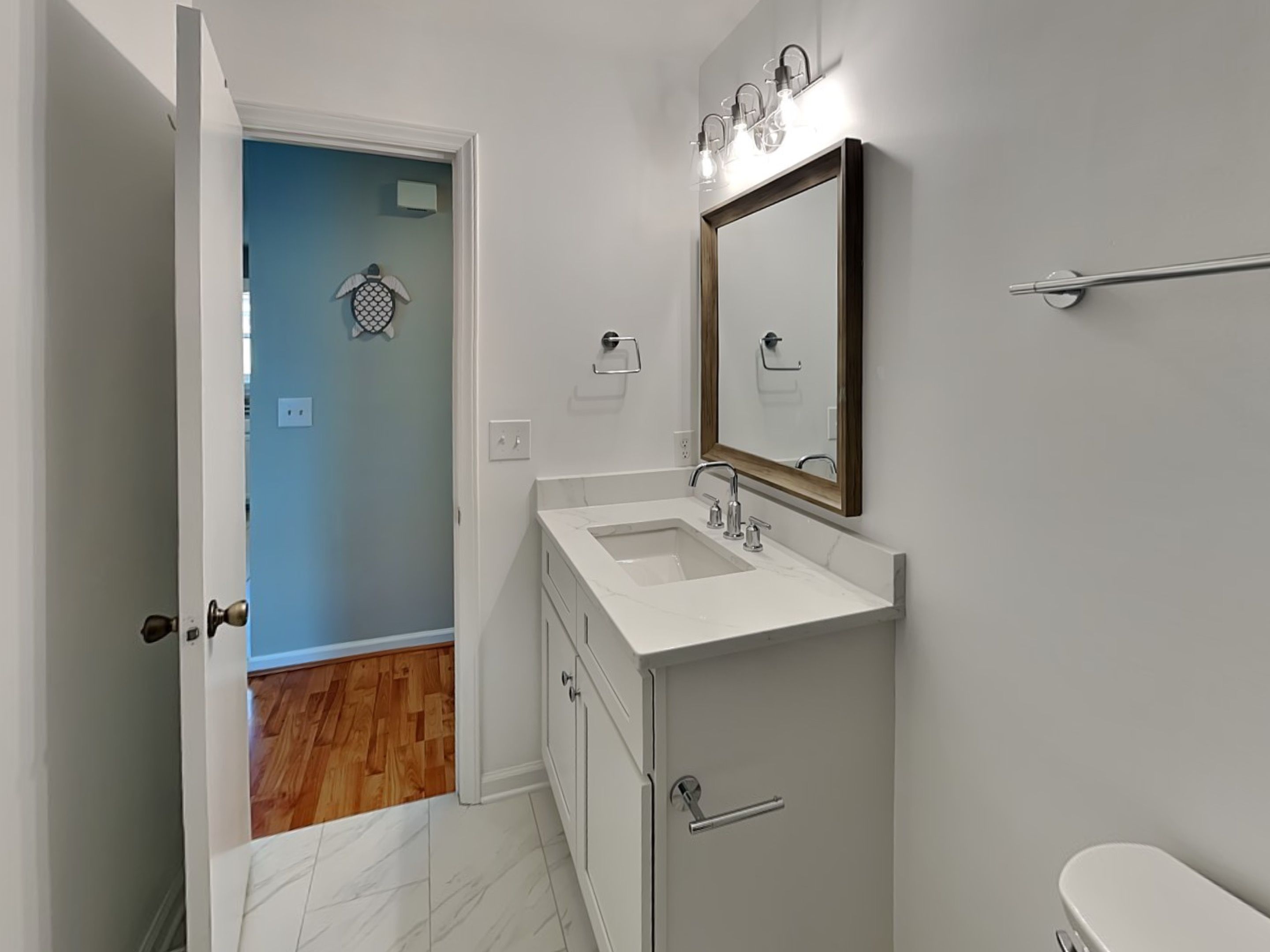 A bathroom with a white sink, mirror, and toilet. There is a wooden floor visible in the background.