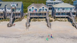 A beachfront property with multiple decks, a sandy beach, and a view of the ocean.