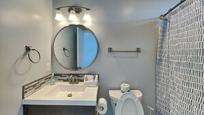 A bathroom with a sink, mirror, toilet, and shower curtain.