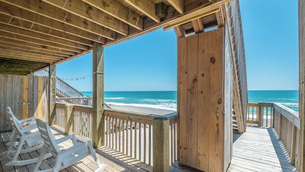 A wooden deck with white rocking chairs overlooking a beach.
