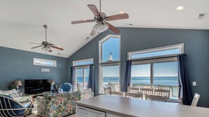 A spacious living room with a large TV, comfortable seating, a kitchen area, and a balcony with ocean views.