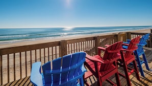 A wooden deck with red and blue Adirondack chairs overlooking a beach.