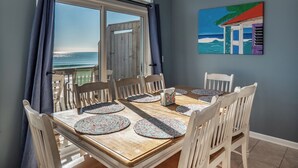 A dining area with a view of the ocean, a painting on the wall, and a wooden table with chairs.