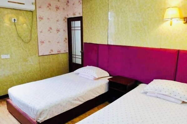 A room with two beds, a wooden floor, a wall-mounted light fixture, and a door with a glass panel. - Kangbao Hotel (Xuzhou)