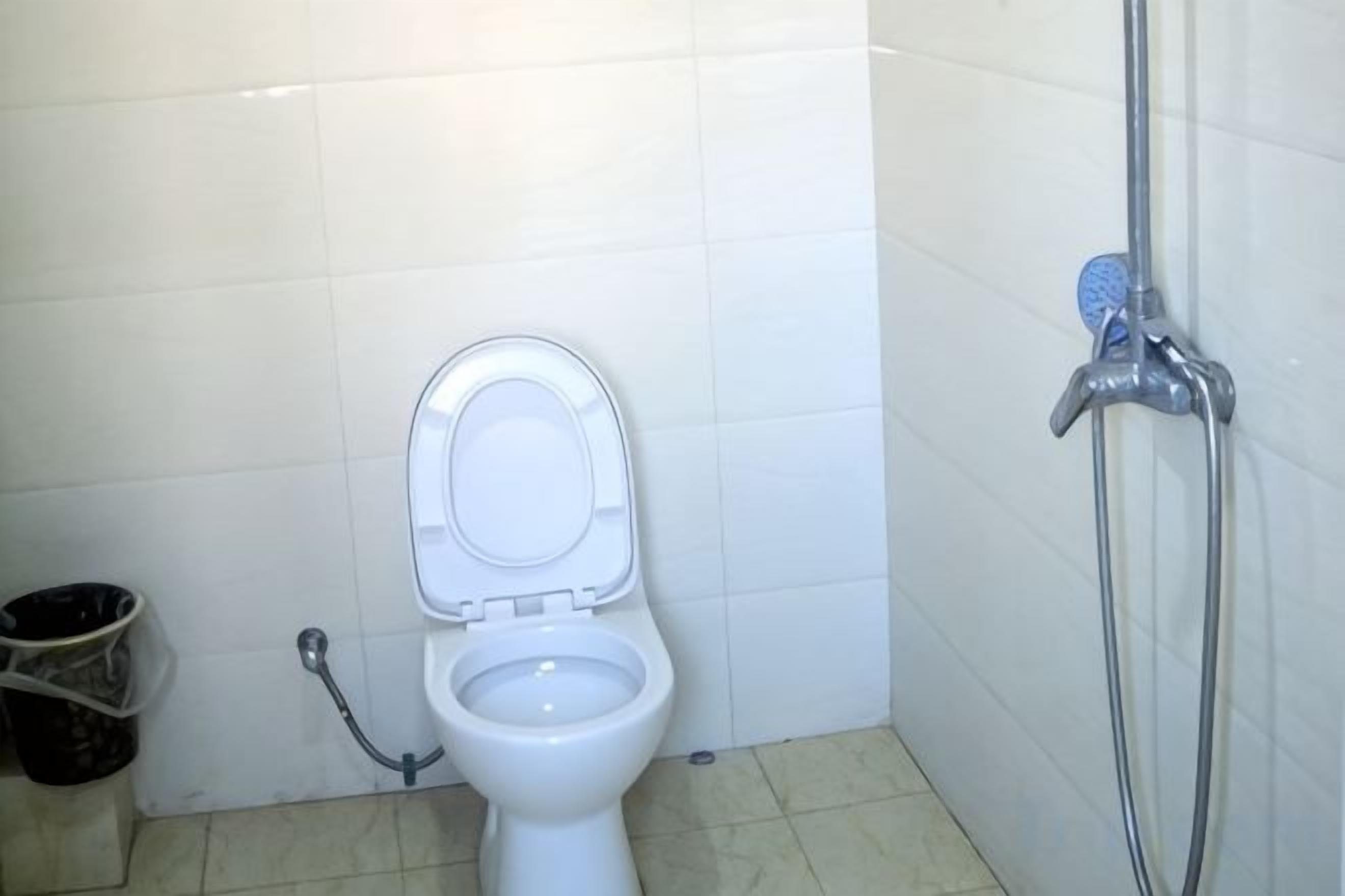 A bathroom with a toilet, a shower, and a trash bin.