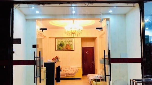 A hotel lobby with a reception desk, a sofa, a chair, a small table with flowers, a chandelier, and a painting on the wall. - Kangbao Hotel (Xuzhou)