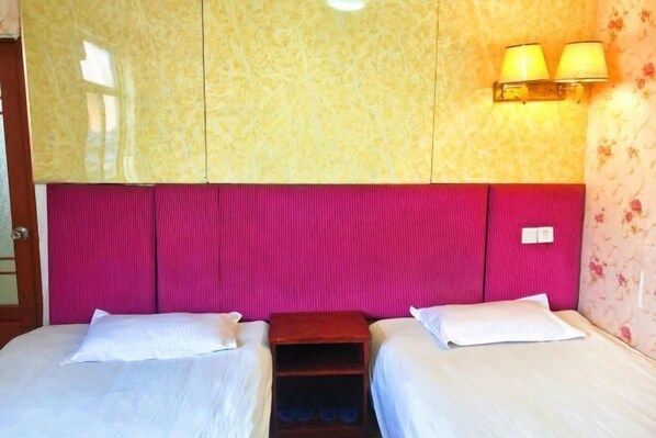 Une chambre d’hôtel avec deux lits, une table de chevet en bois et une lampe fixée au mur.