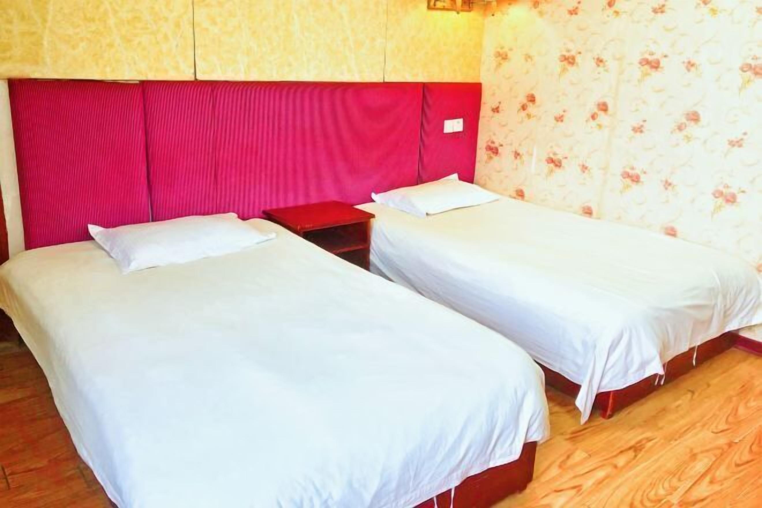 Une chambre avec deux lits simples, un plancher en bois et une tête de lit rouge.