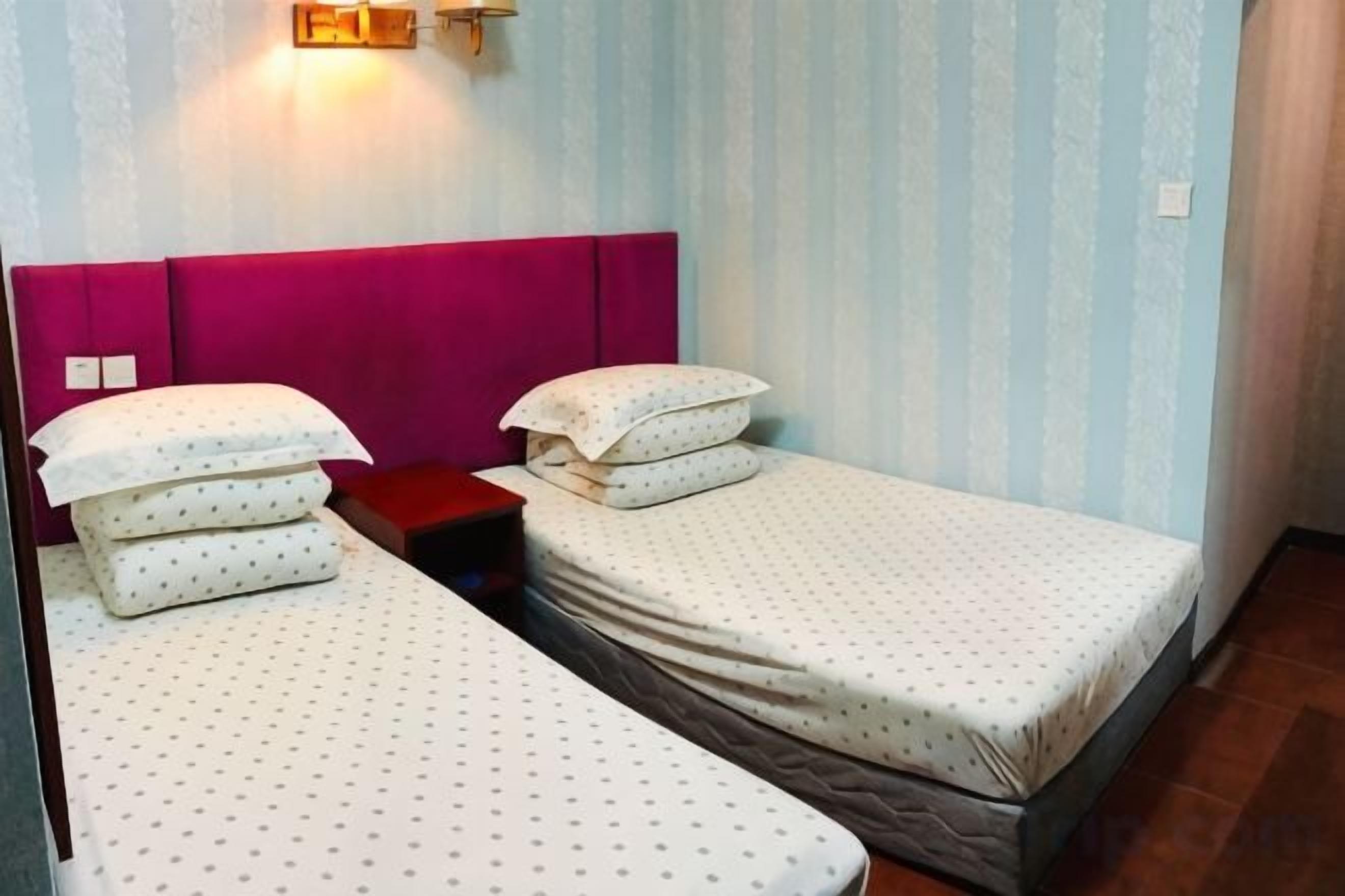 Et hotelværelse med to senge, et natbord og en lampe på væggen.