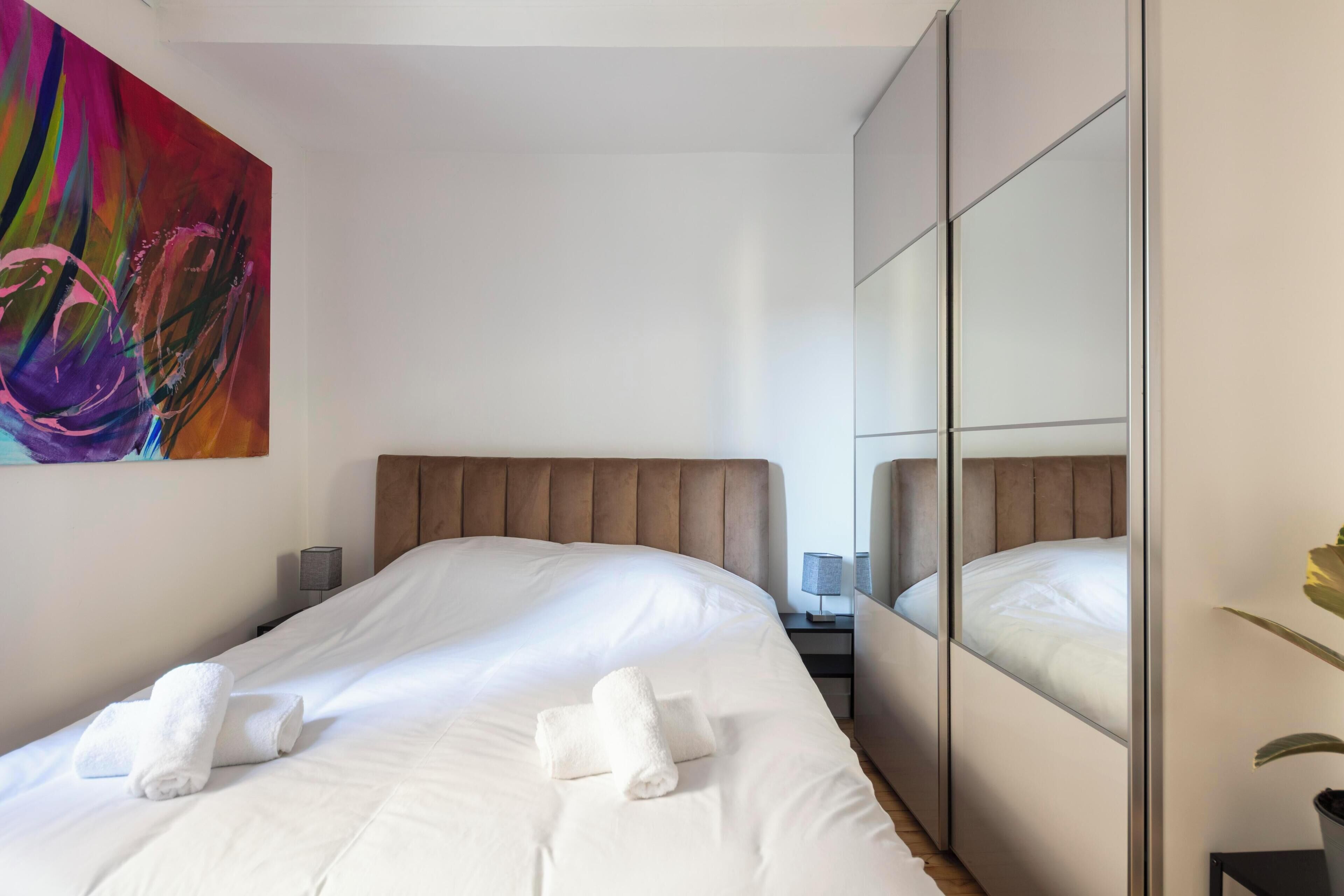 Ein Hotelzimmer mit einem großen Bett, einem Kopfteil, einem Nachttisch mit Lampe und einem Spiegel.