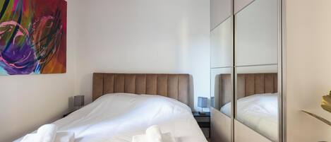 Ein Hotelzimmer mit einem großen Bett, einem Kopfteil, einem Nachttisch mit Lampe und einem Spiegel.