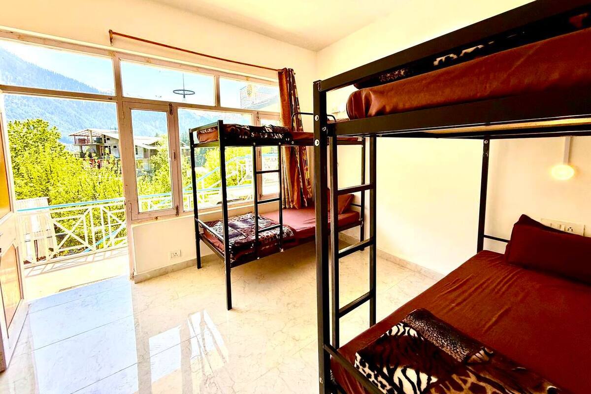 Une chambre avec des lits superposés, un balcon offrant une vue sur la verdure et les montagnes, et une grande fenêtre.