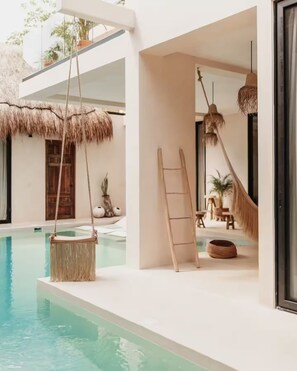 A modern pool area with a hanging chair, a ladder, and a hammock. - Villa Aura → Swim-up rooms, Private Pool & Rooftop (Tulum)