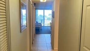 A hallway with a ceiling light, a door on the right, and a view of a balcony with outdoor furniture.