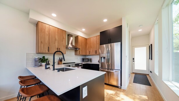 Una cocina moderna con armarios de madera, electrodomésticos de acero inoxidable y una isla blanca con taburetes de bar.