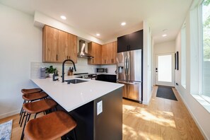 A modern kitchen with wooden cabinets, stainless steel appliances, and a white island with bar stools. - Central Seattle Nearby Downtown and Stadiums with A/C, Parking & Transit Access (Seattle)