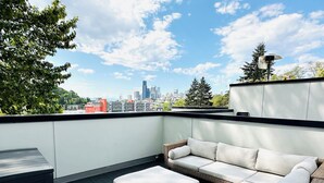 Una terraza en la azotea con un sofá y reposapiés de mimbre, una mesita y vistas a la ciudad.