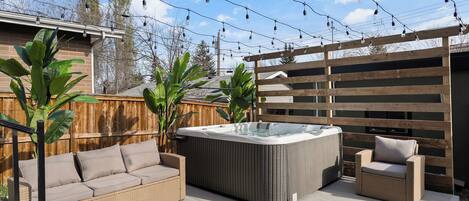 Een achtertuin met een hottub, een rieten bank en een houten terras.