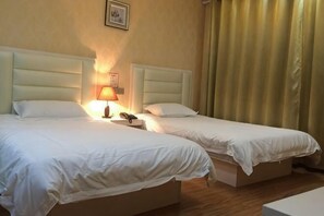 Twee enkele bedden met witte lakens, een nachtkastje met een lamp, en een lijst met een afbeelding aan de muur.