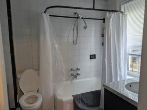 Ein Badezimmer mit Badewanne, Toilette und einem Fenster mit Jalousien.