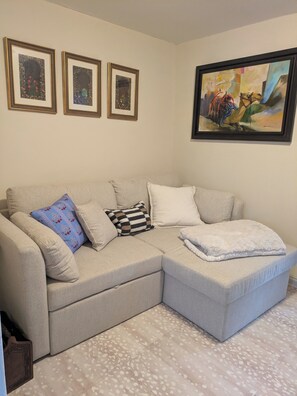 A living room with a beige sectional sofa, three framed artworks, and a large painting on the wall.