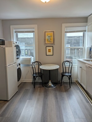A compact kitchen with a round table, two chairs, a washing machine, and a refrigerator.