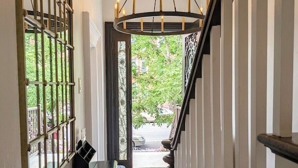 Un pasillo con escaleras, una araña y vistas al exterior con vegetación.
