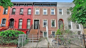Una hilera de casas urbanas de tres pisos, con una cerca metálica al frente, cada una con puerta principal y ventanas.