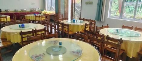 A dining area with round tables and chairs, large windows, and a view of the outdoors.