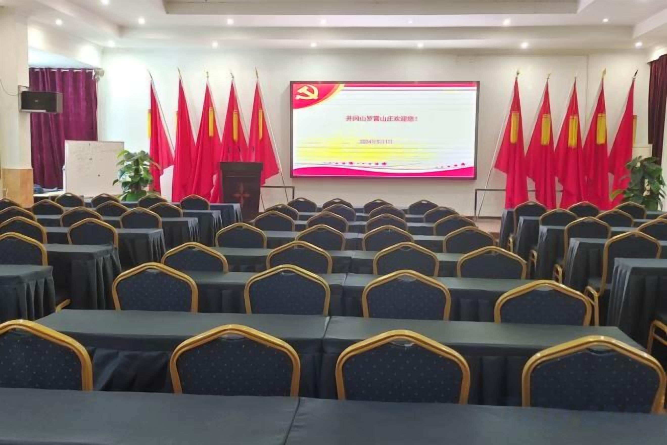 A conference room with rows of tables and chairs, a presentation screen, and red flags.
