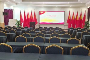 A conference room with rows of tables and chairs, a presentation screen, and red flags. - Luoxiao Mountain Villa Jinggangshan (Jinggangshan City)