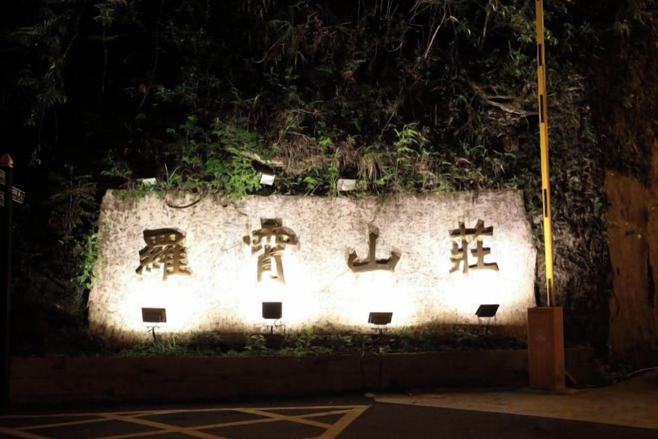 A wall with illuminated characters, a paved area, and a wooden structure.