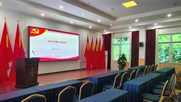 A conference room with a large screen, rows of tables, and red flags.
