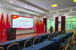 A conference room with a large screen, rows of tables, and red flags. - Luoxiao Mountain Villa Jinggangshan (Jinggangshan City)