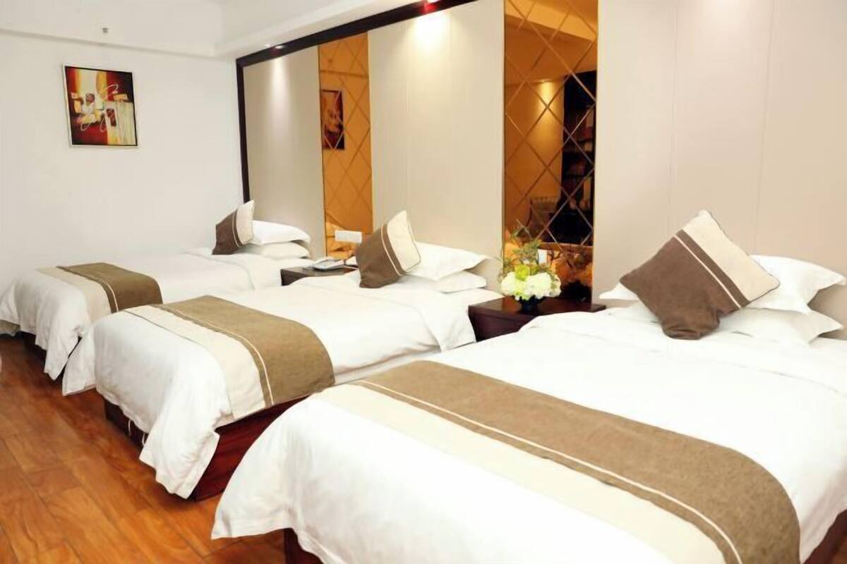 A hotel room with three beds, a large mirror, and a wooden floor.