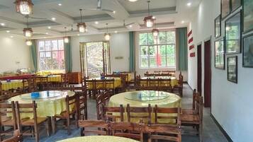 A dining area with round tables and chairs, large windows, and ceiling fans.
