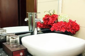 Un baño con un lavamanos blanco, un grifo cromado y un florero con flores rojas y blancas.