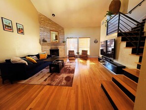 Un salón amplio con chimenea de ladrillo, una escalera y un televisor grande.