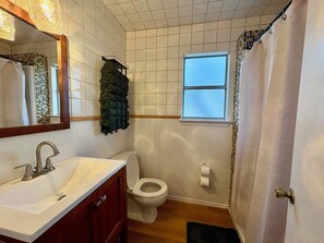 Une salle de bain avec un lavabo blanc, des toilettes, une fenêtre et un rideau de douche.