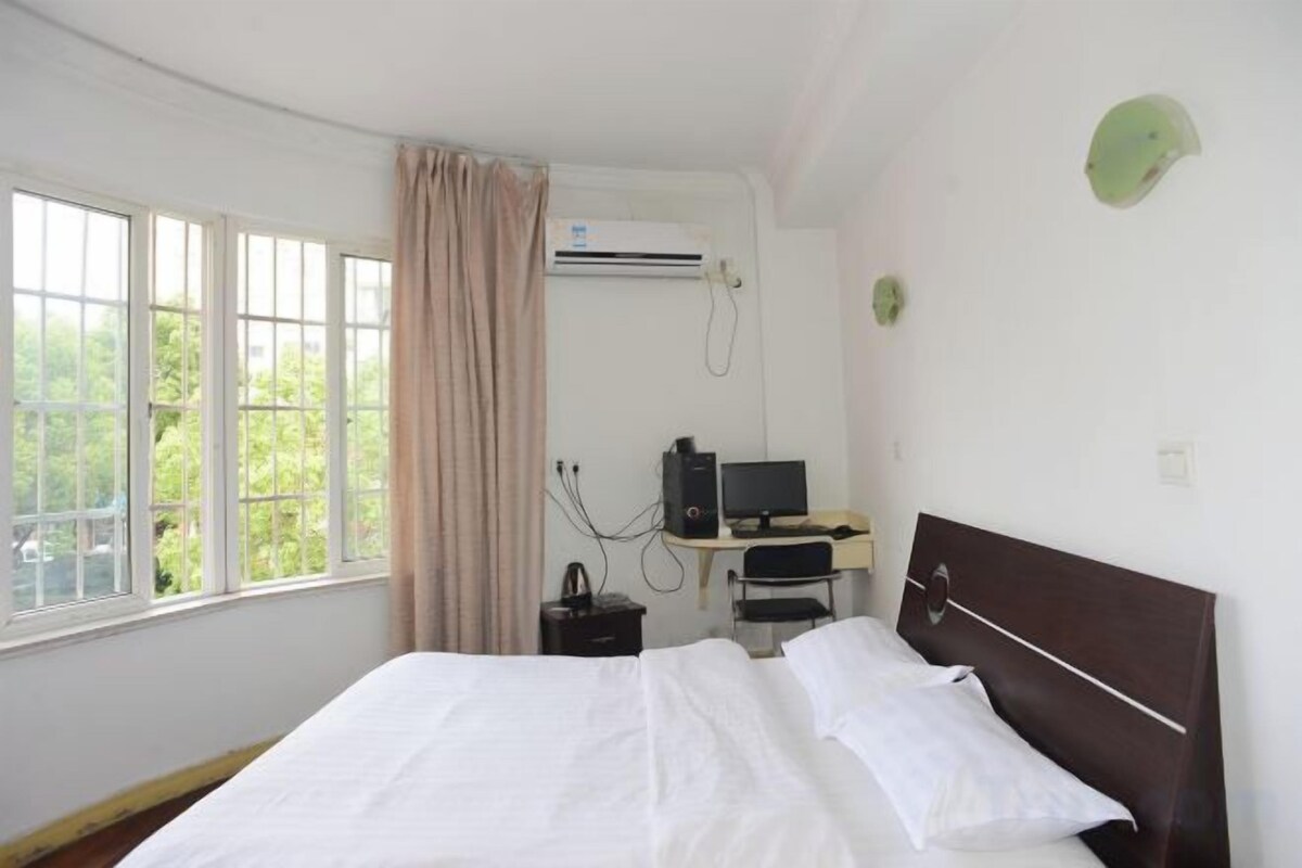 A hotel room with a bed, a desk with a computer, and a window with curtains.