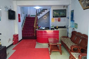 Zona de recepción con un escritorio rojo, una escalera y un sofá.
