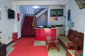 A reception area with a red counter, wooden furniture, a staircase, and a television on the wall. - Yuanyuan Hostel (Shanghai)