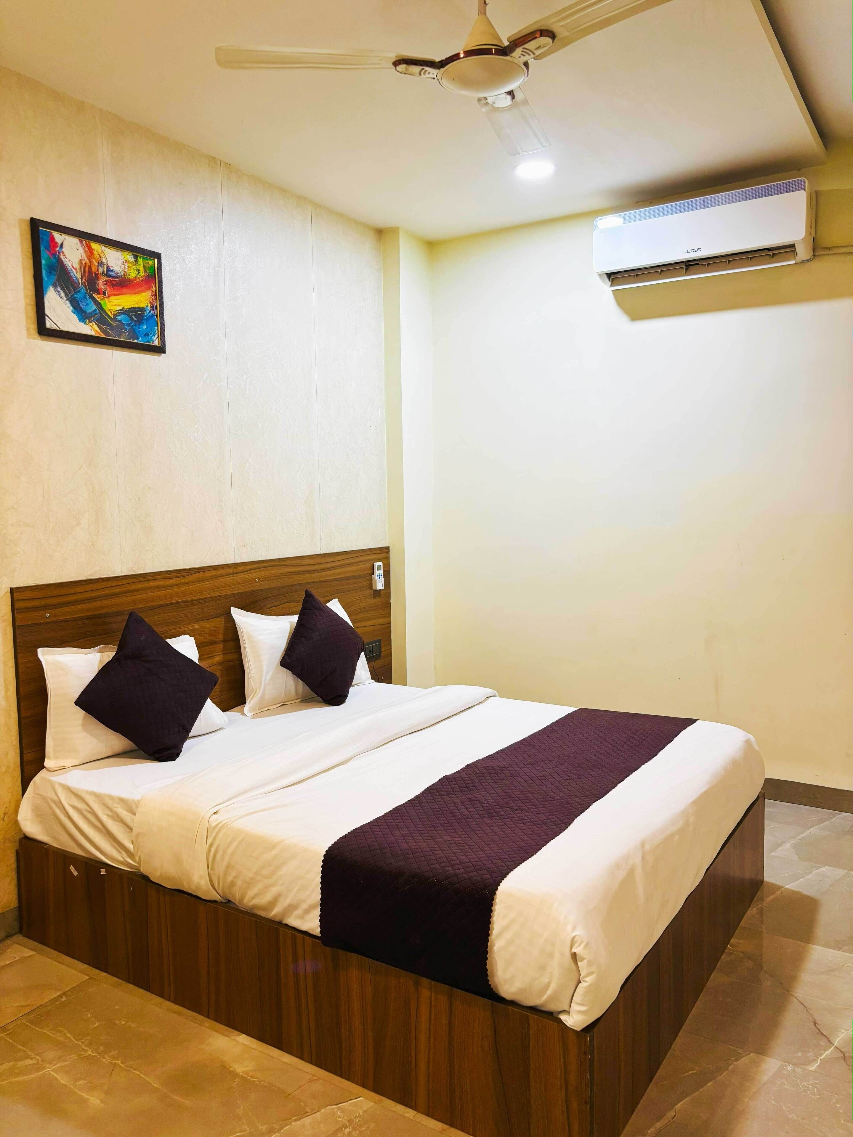 Un lit bien fait, avec une tête de lit en bois, un ventilateur de plafond et un appareil de climatisation fixé au mur.